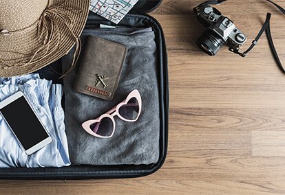 Open suitcase with travel items laid out on a wooden floor.